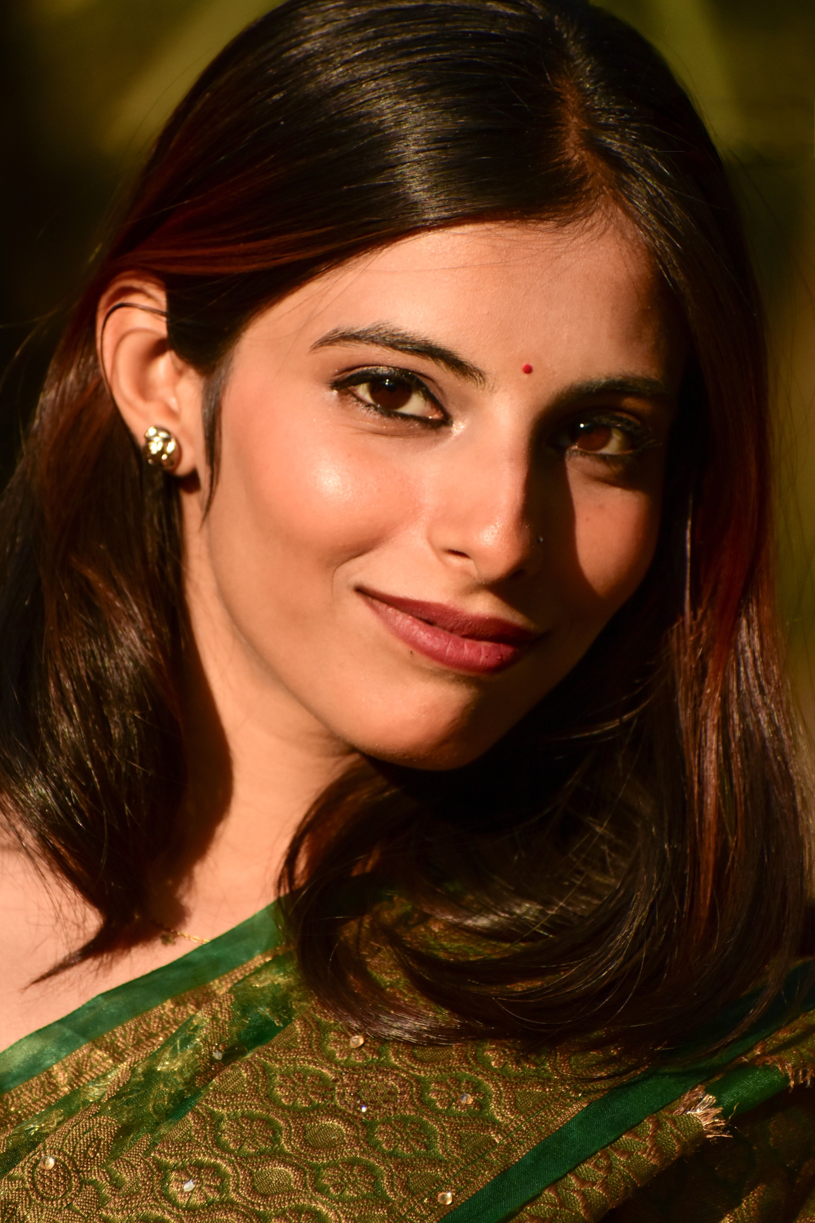 Portrait of a smiling Indian woman wearing a green saree, symbolizing elegance and cultural grace.