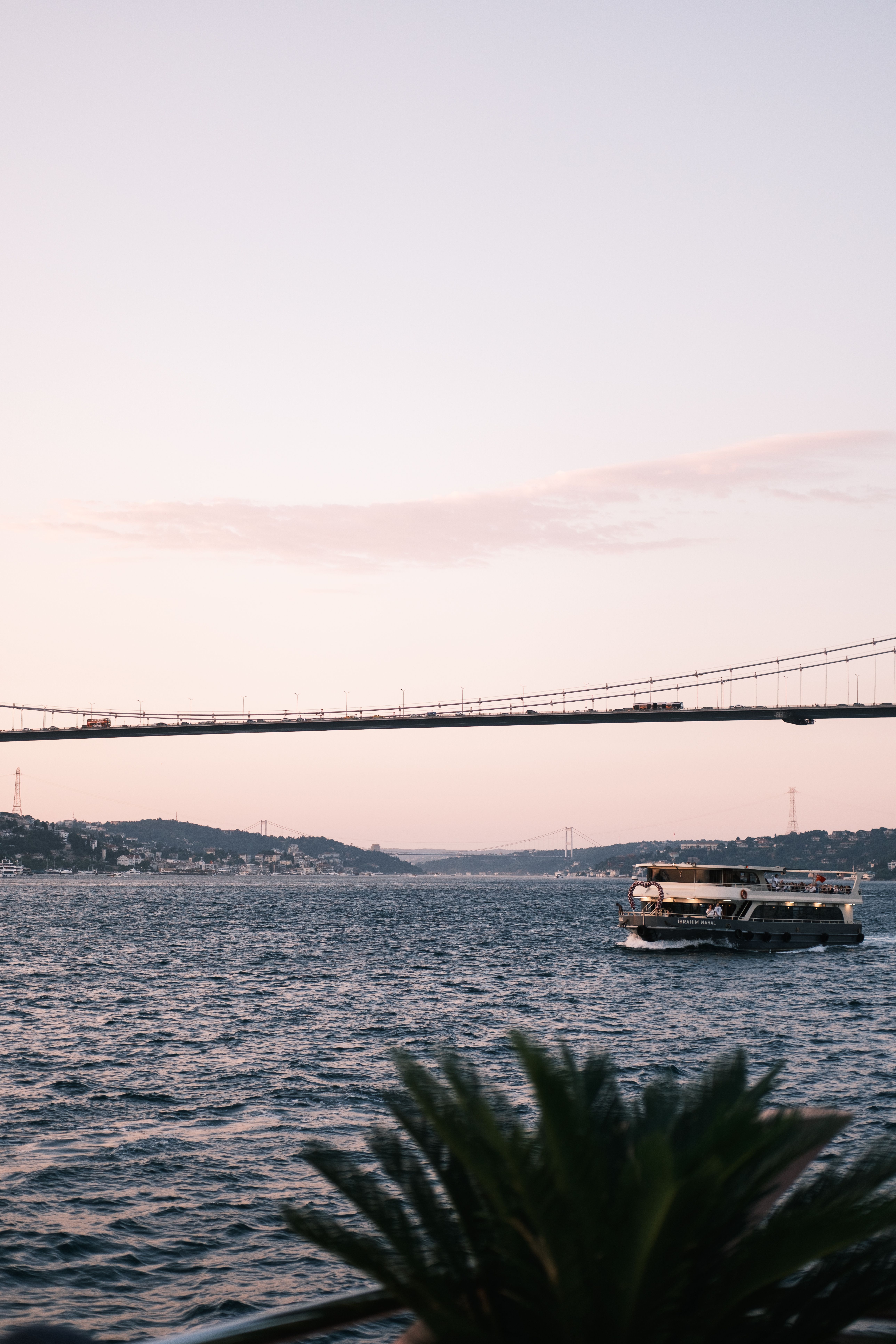 Scenic view of the Bosphorus Strait featuring a bridge and boat during sunset in Istanbul, Türkiye.