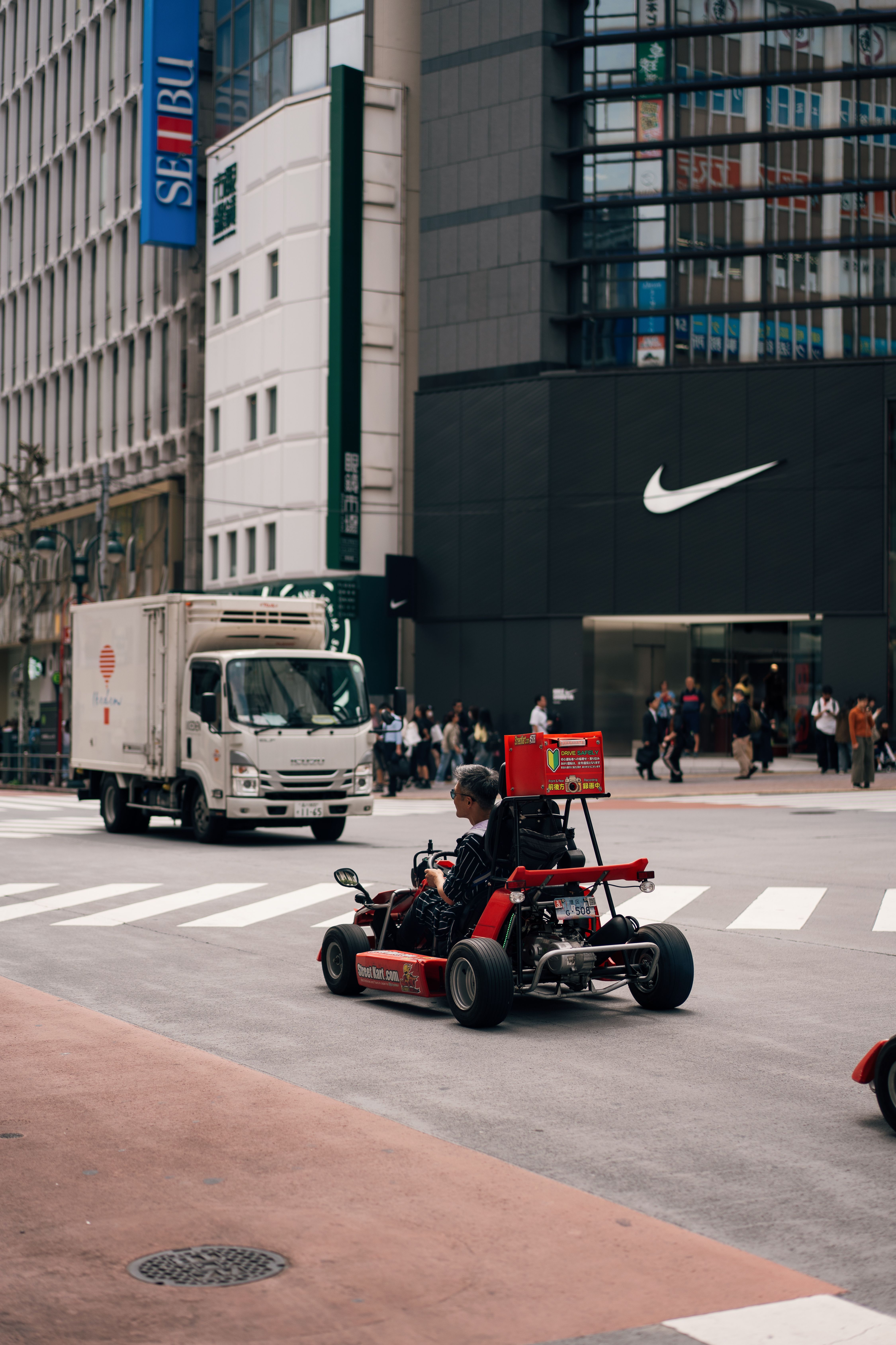 A red go-kart driving on a bustling Tokyo street with iconic buildings.