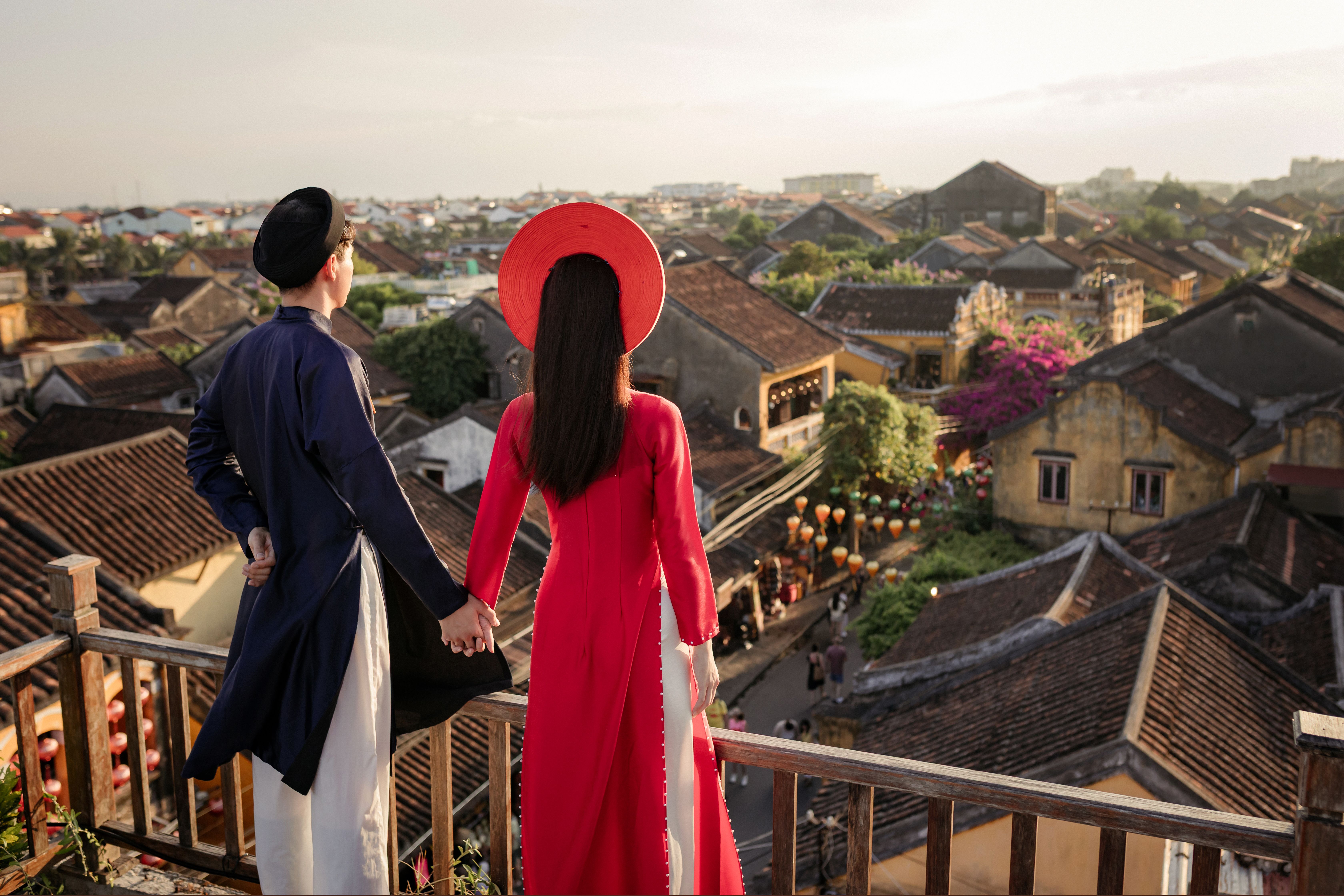 Couple in Vietnamese traditional clothing enjoying the scenic view of Hội An's historic rooftops.