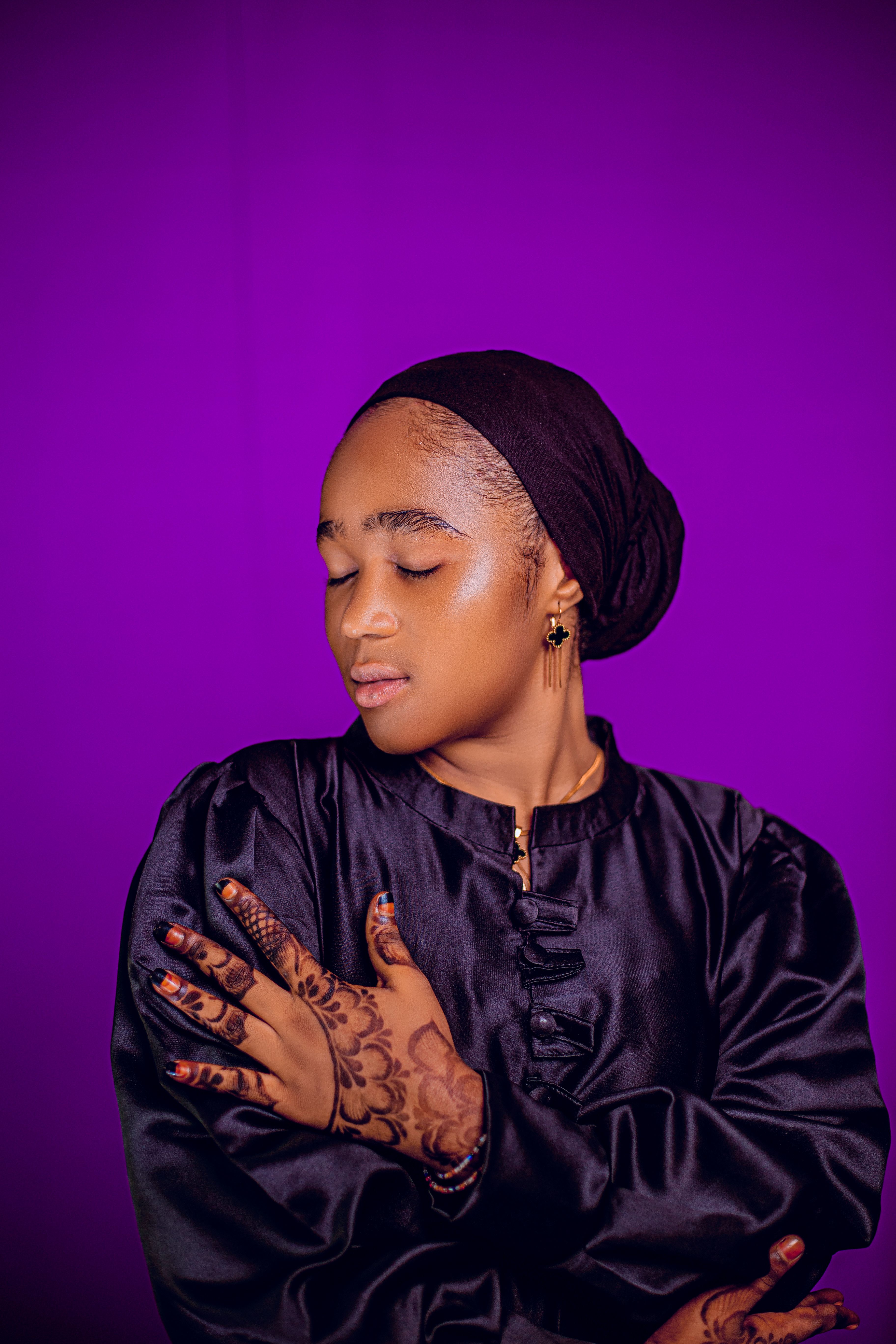 A serene woman with henna designs poses against a vivid purple backdrop.