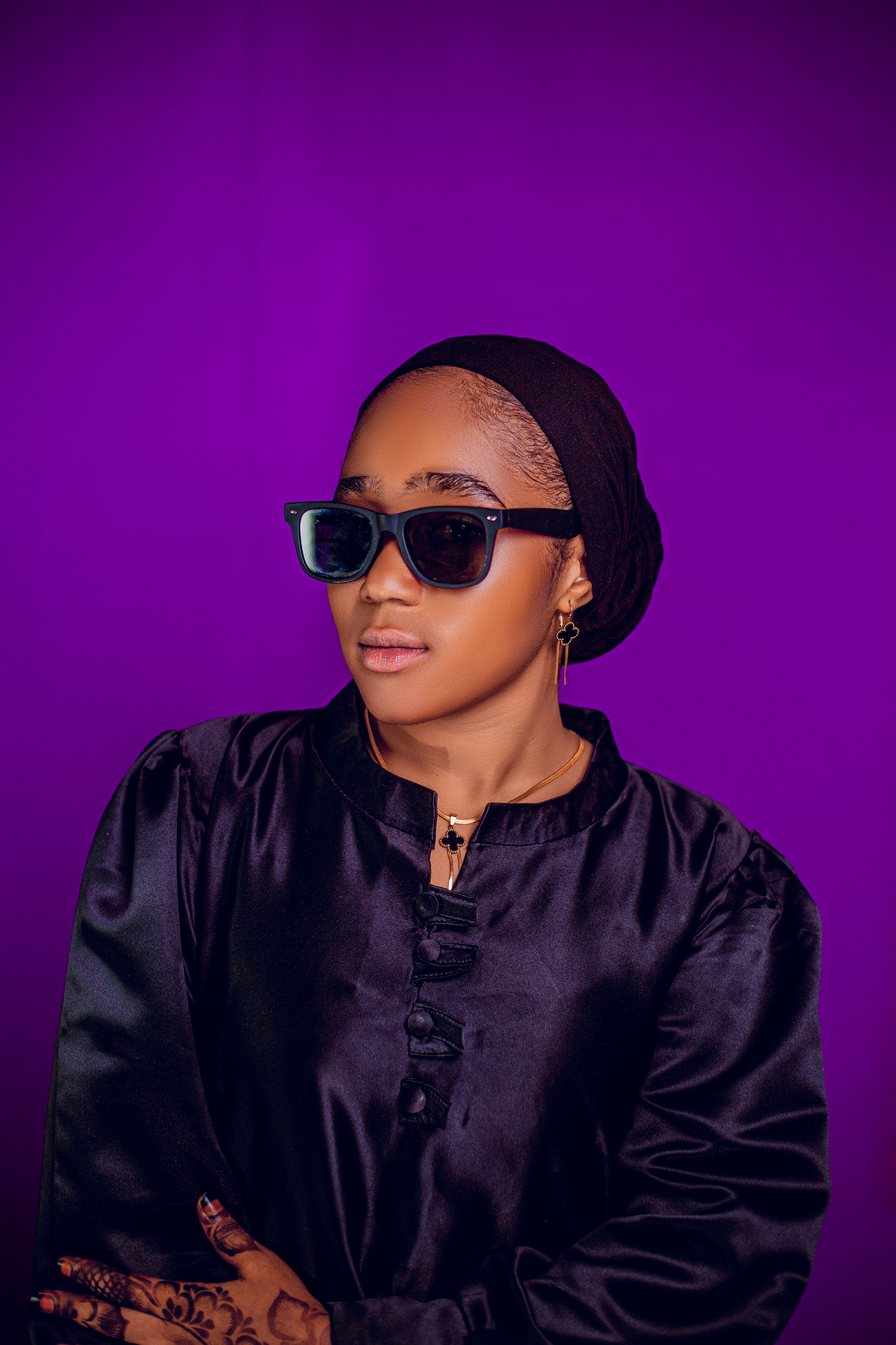 Stylish woman wearing sunglasses with a purple backdrop, radiating confidence.