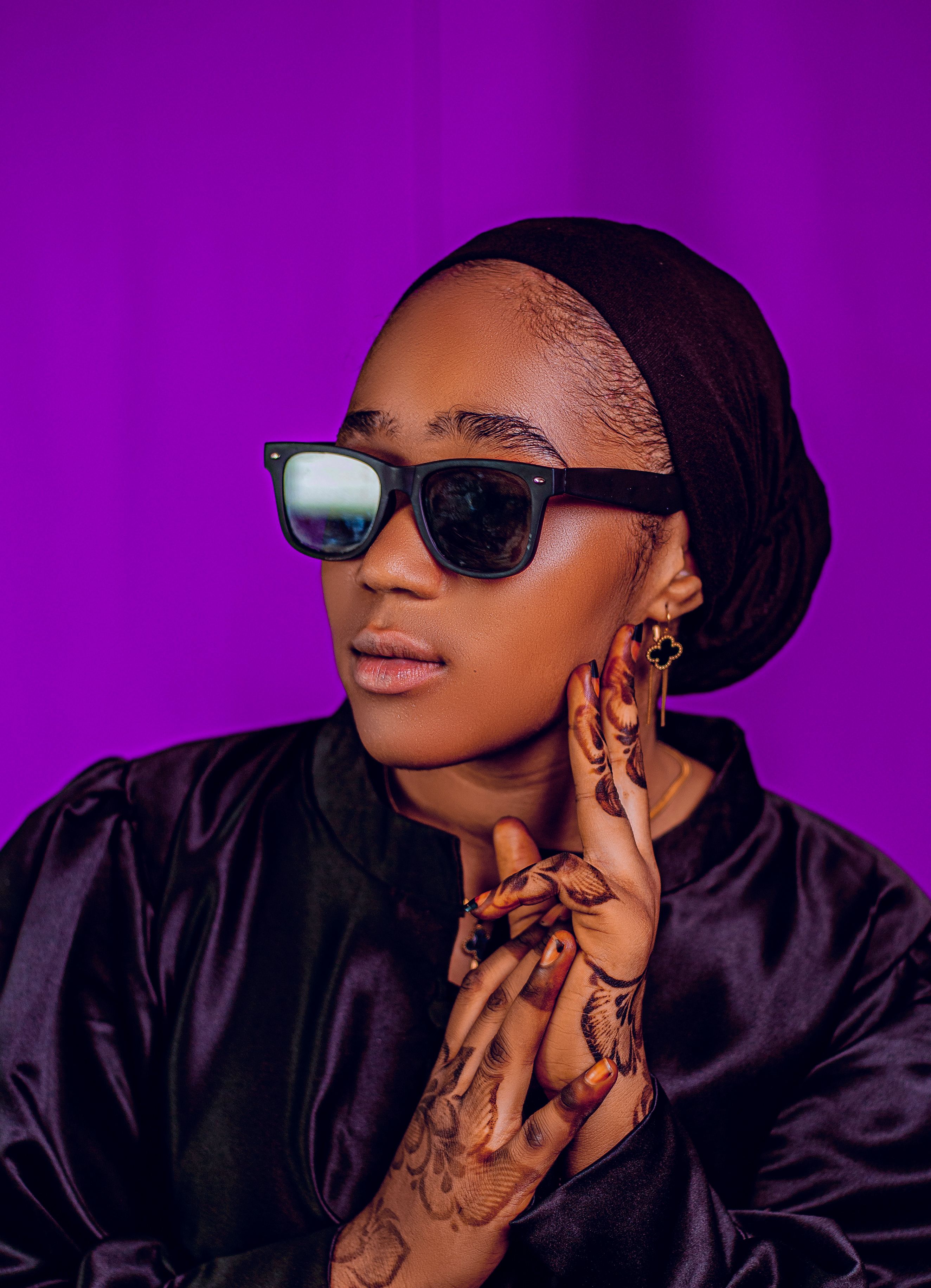 Fashionable portrait of a woman in sunglasses with intricate henna design on hands.