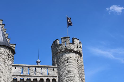 A medieval castle tower with a flag under a clear blue sky in Antwerp, Belgium.