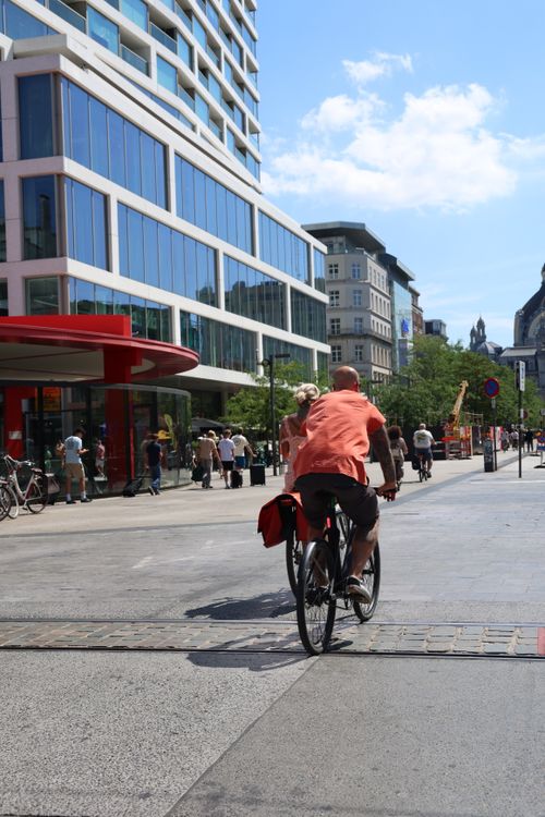 Free A cyclist rides through a vibrant city street in Antwerp, Belgium, under a clear blue sky. Stock Photo