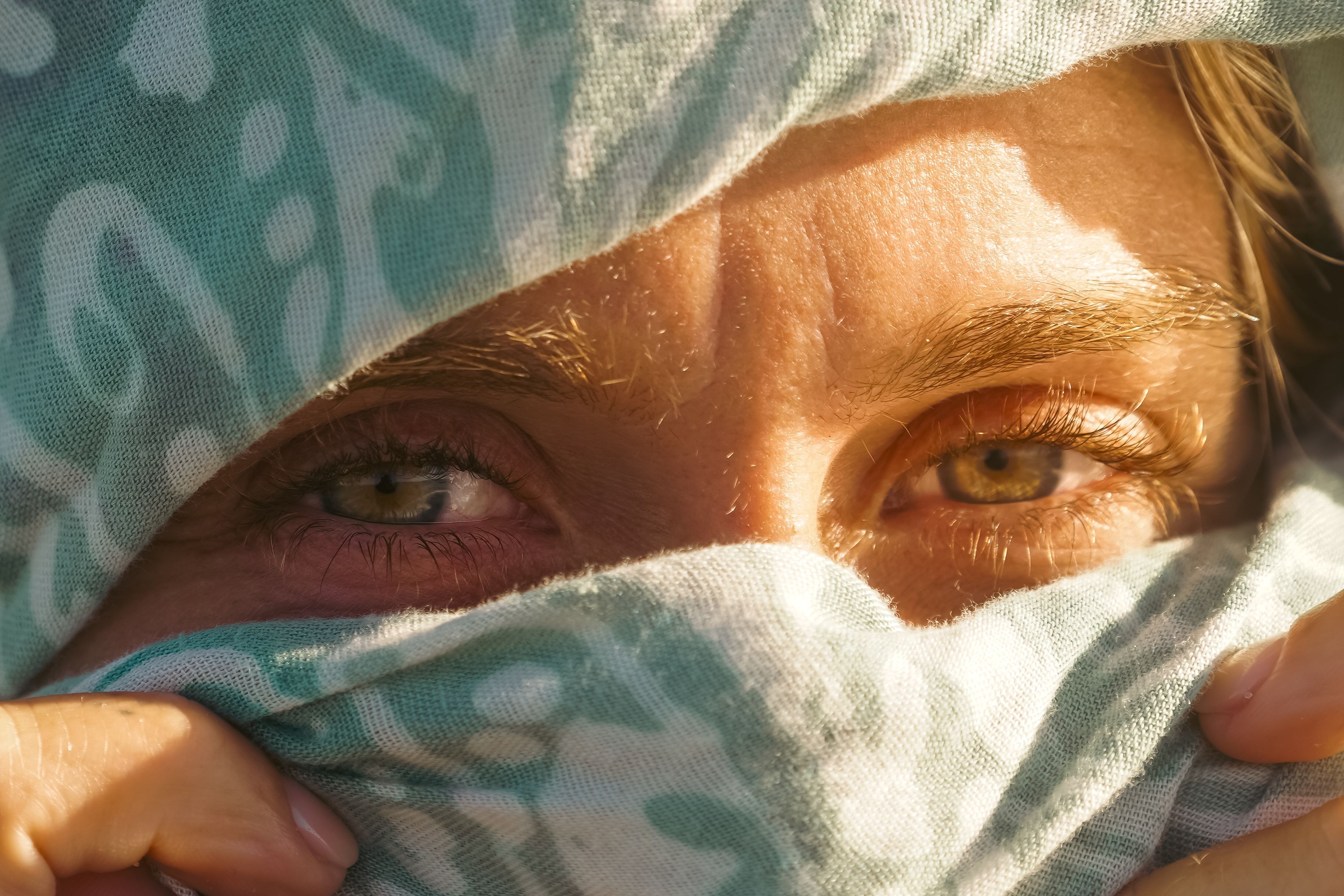 Close-up of captivating eyes behind a patterned blue scarf in natural light.