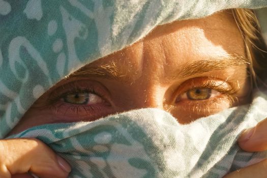 Close-up of captivating eyes behind a patterned blue scarf in natural light.