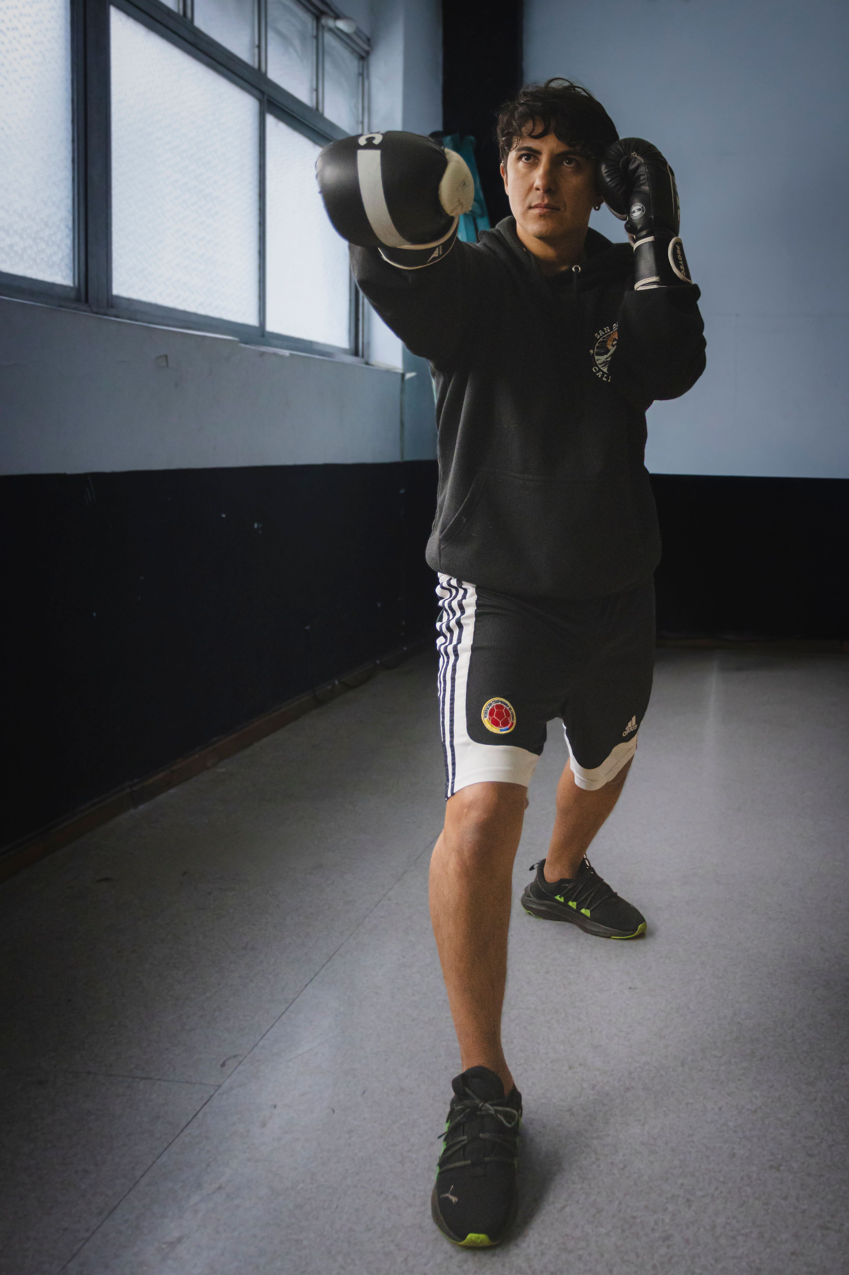 A young Hispanic boxer practicing punches inside a gym, focusing on technique.