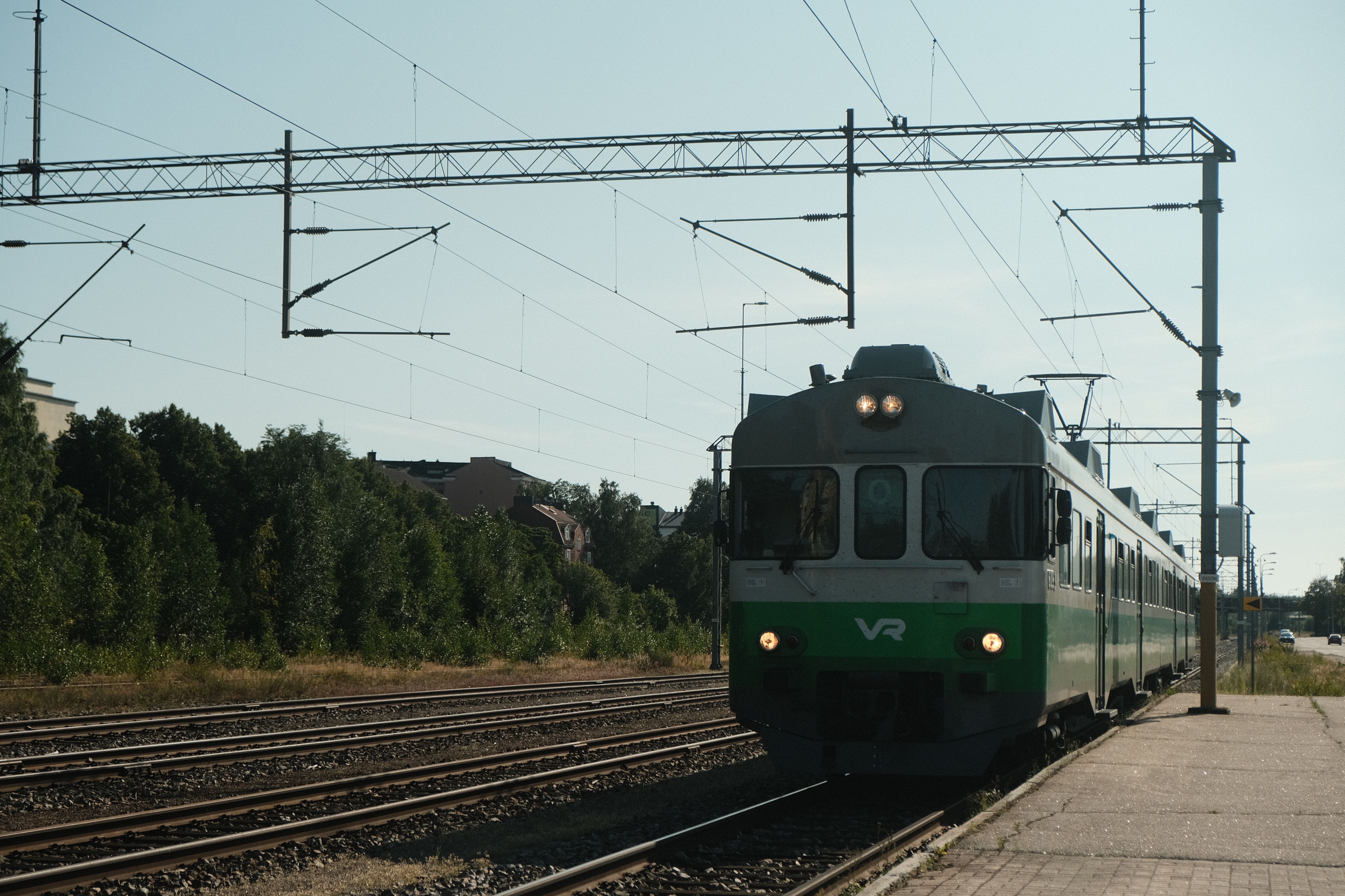 A green train approaches a platform on a clear day, showcasing urban transit and infrastructure.