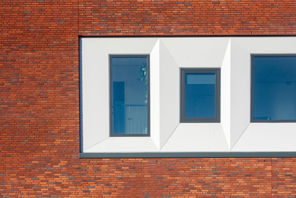 Three white aluminium windows projecting from a red brick office facade