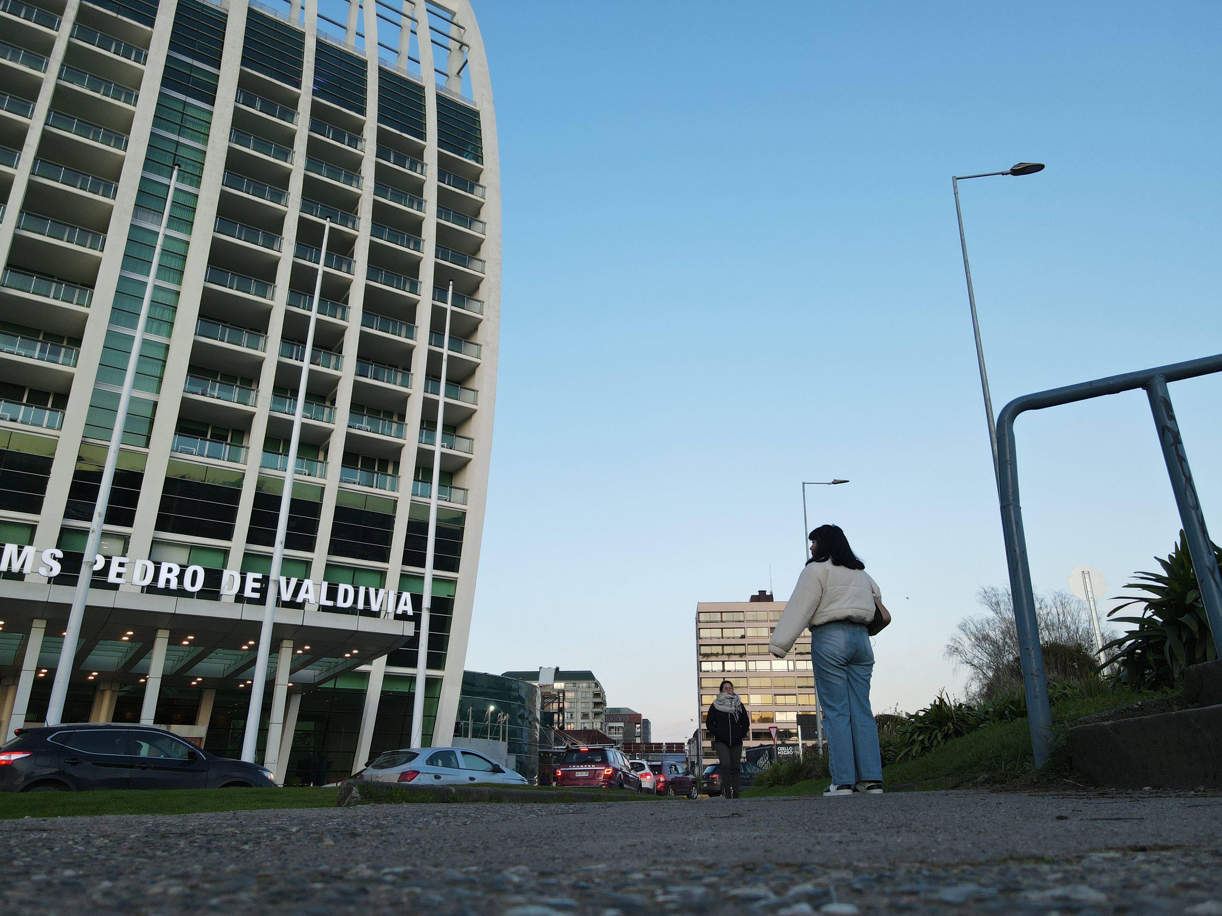 A modern urban street scene in Valdivia with pedestrians and high-rise building under clear sky.