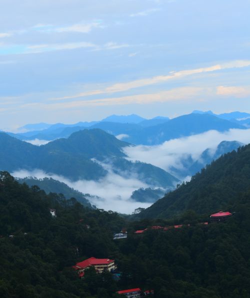Free Captivating view of misty valleys in the Himalayas, surrounded by lush greenery and red-roofed buildings. Stock Photo