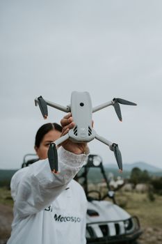 A woman in a white jacket holding a drone in an outdoor environment, suggesting adventure.