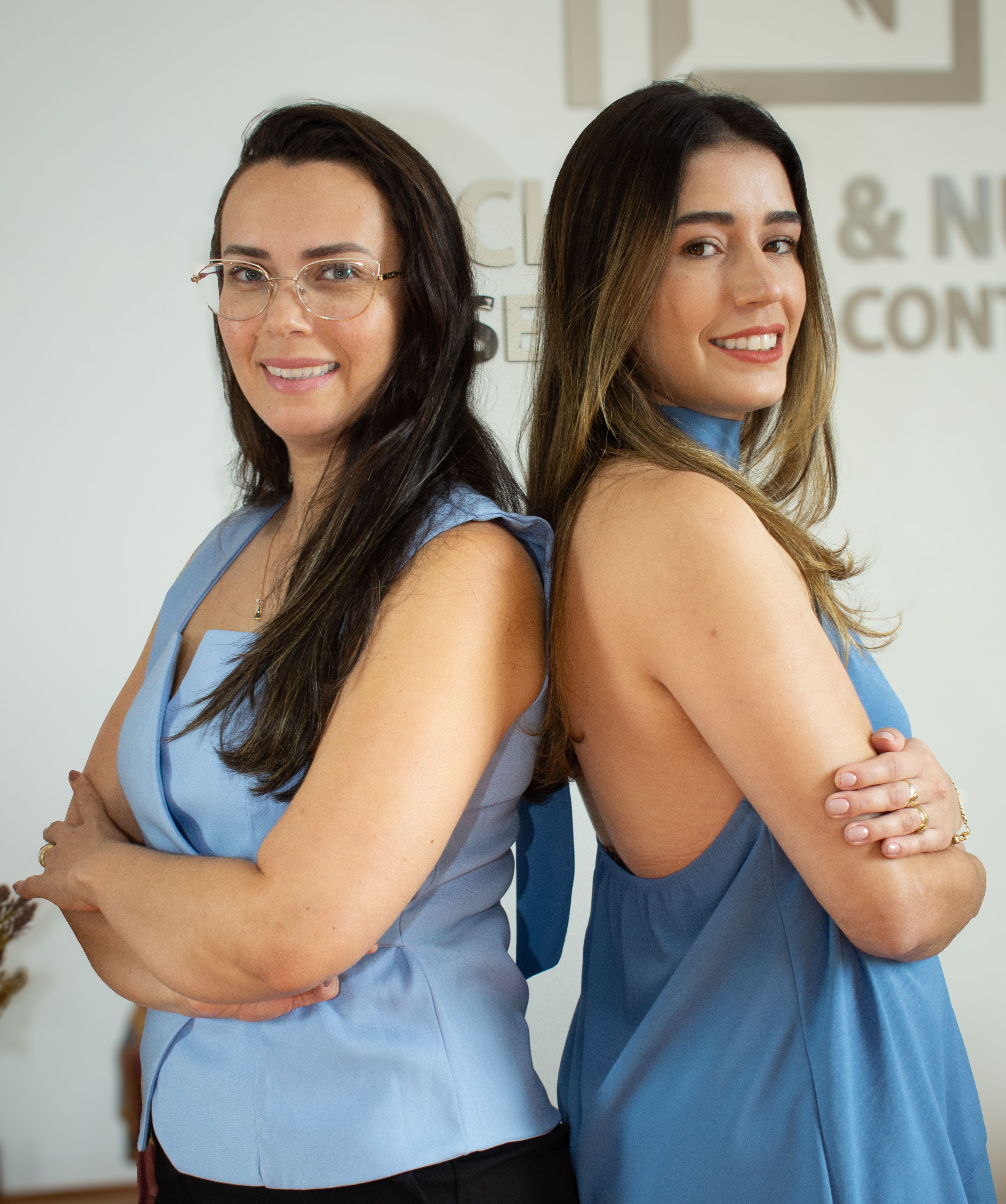 Two professional women standing back to back in an office setting, expressing confidence and teamwork.