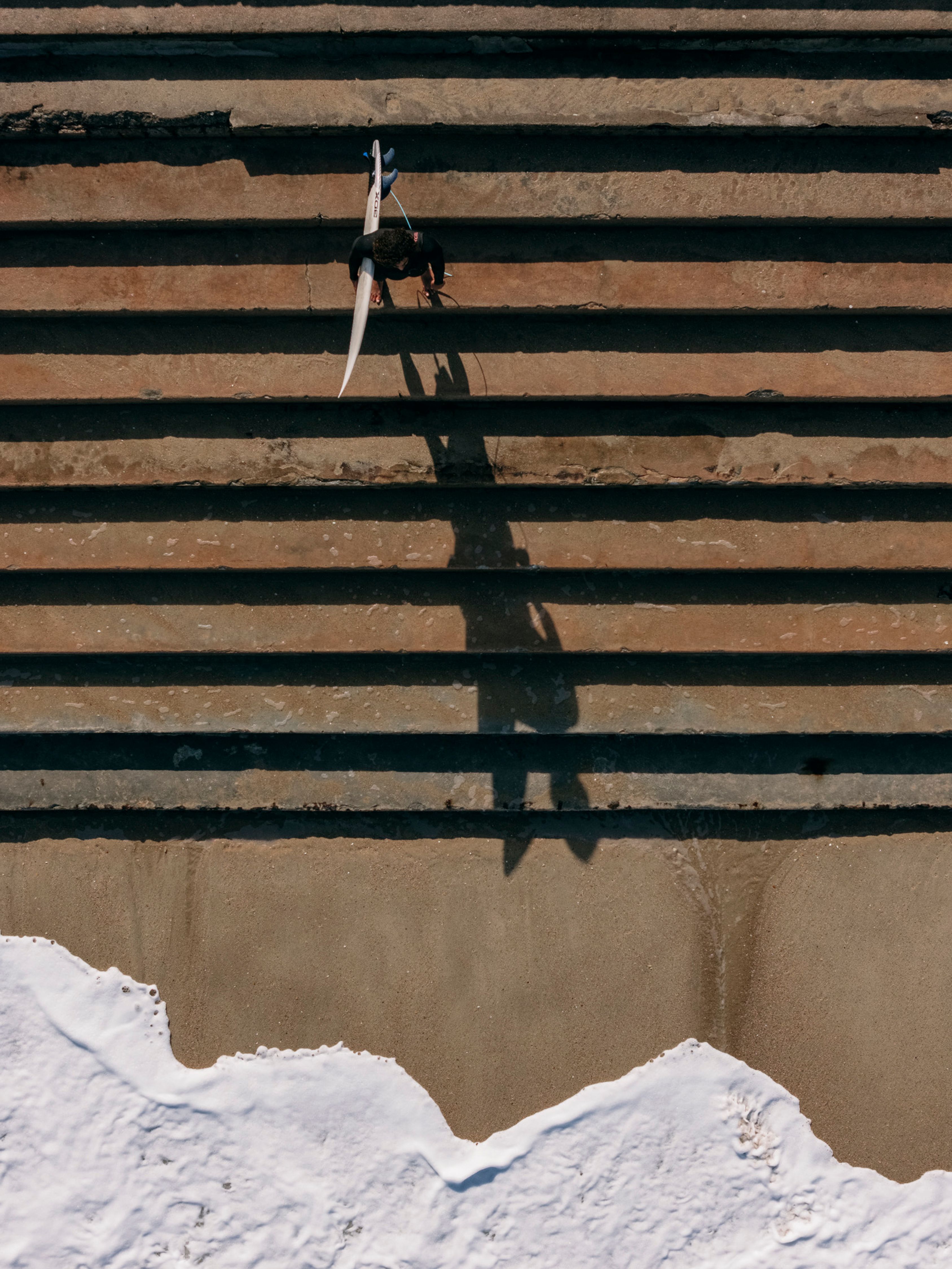 Aerial shot of a surfer carrying a surfboard on stairs along the beach in Rio de Janeiro.