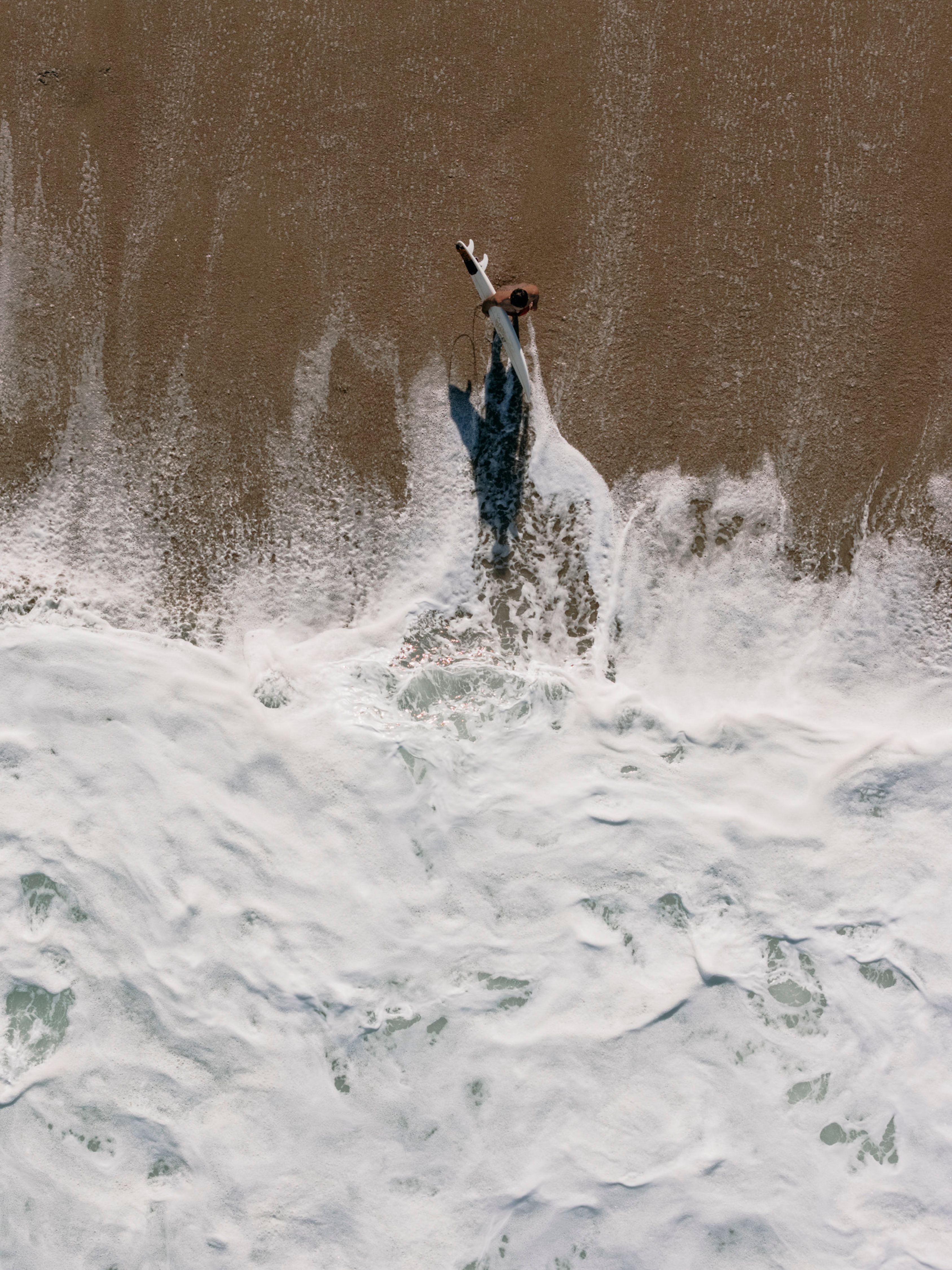 Aerial view of a surfer walking along the beach in Rio de Janeiro, capturing the essence of summer.