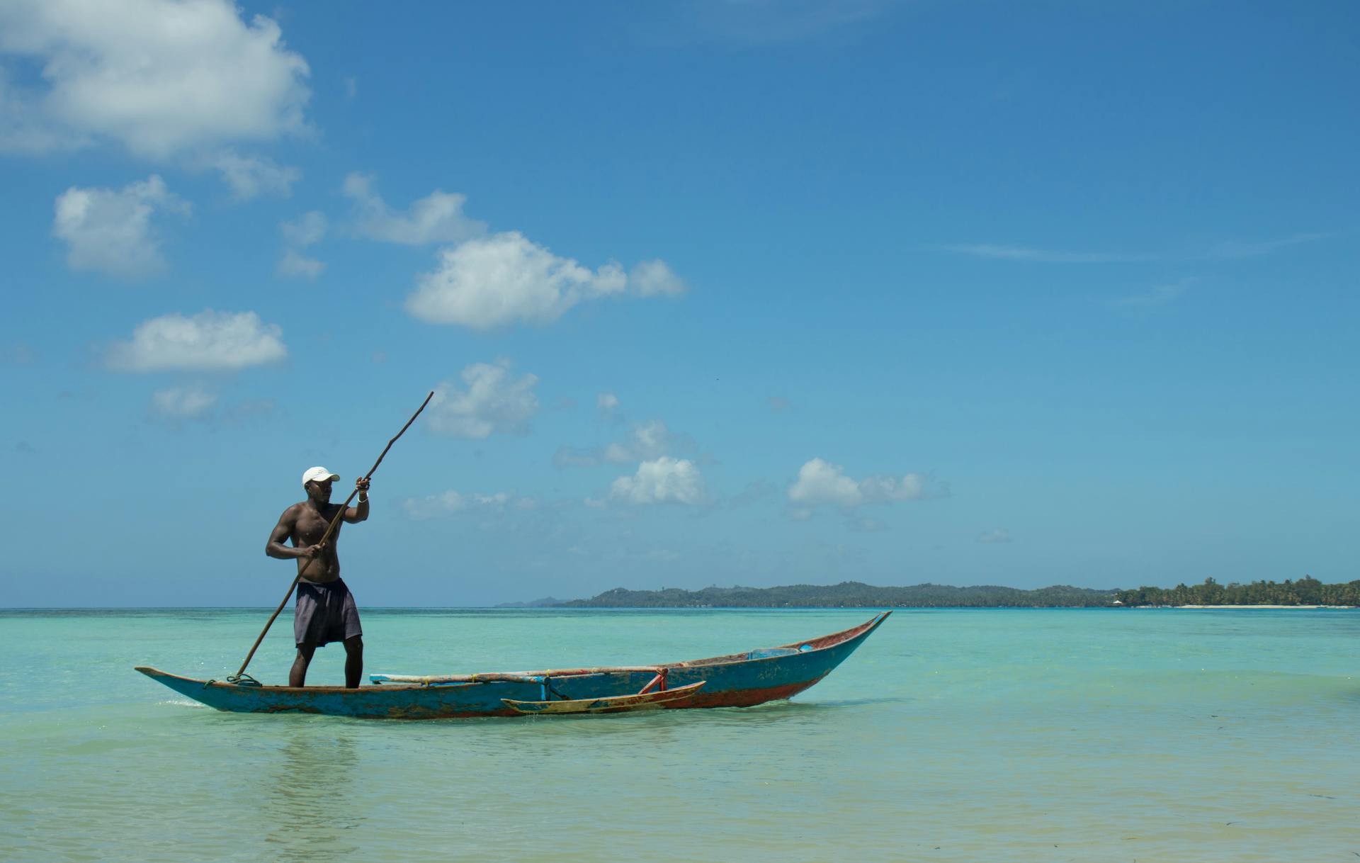 A fisherman paddles a traditional canoe in the clear waters of Madagascar under a blue sky.