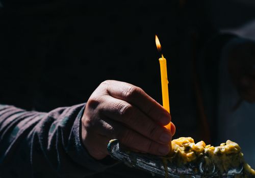 Free Close-up of a hand lighting a yellow candle on a dark background, symbolizing peace and meditation. Stock Photo