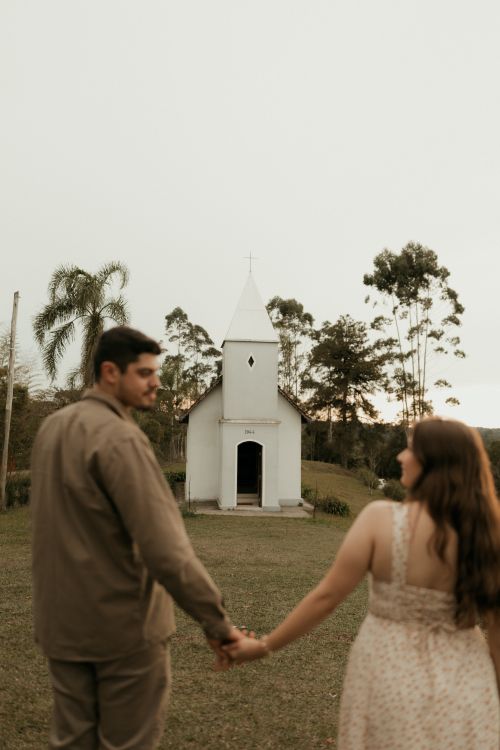 Free Romantic couple holding hands near a small chapel surrounded by nature at sunset. Stock Photo