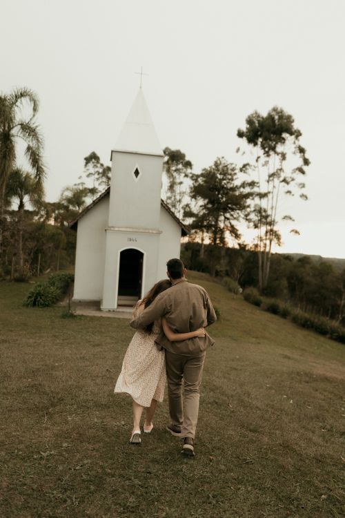 Free Couple walking arm in arm towards a small, scenic chapel at sunset. Stock Photo