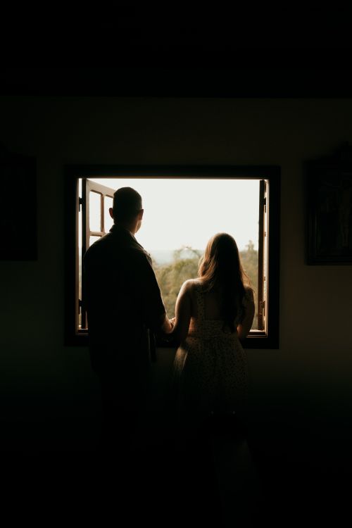 Free Silhouetted couple stands by an open window, admiring a scenic outdoor view. Stock Photo