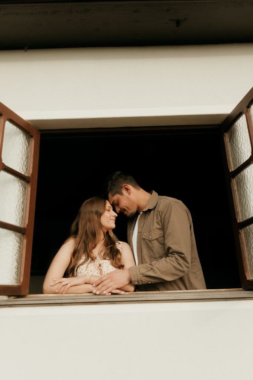 Free A loving couple shares an intimate moment at an open window, creating a warm and romantic ambiance. Stock Photo
