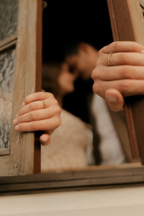 Free Close-up of couple with wedding bands, sharing a tender moment behind a window. Stock Photo