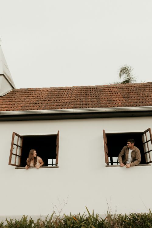 Free A young man and woman smiling at each other from open windows in a quaint building. Stock Photo
