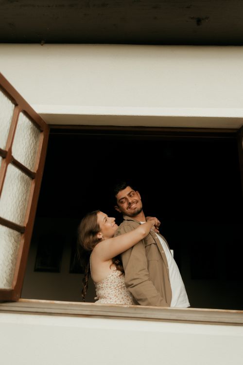 Free A couple shares a joyful moment while looking out from an open window. Stock Photo