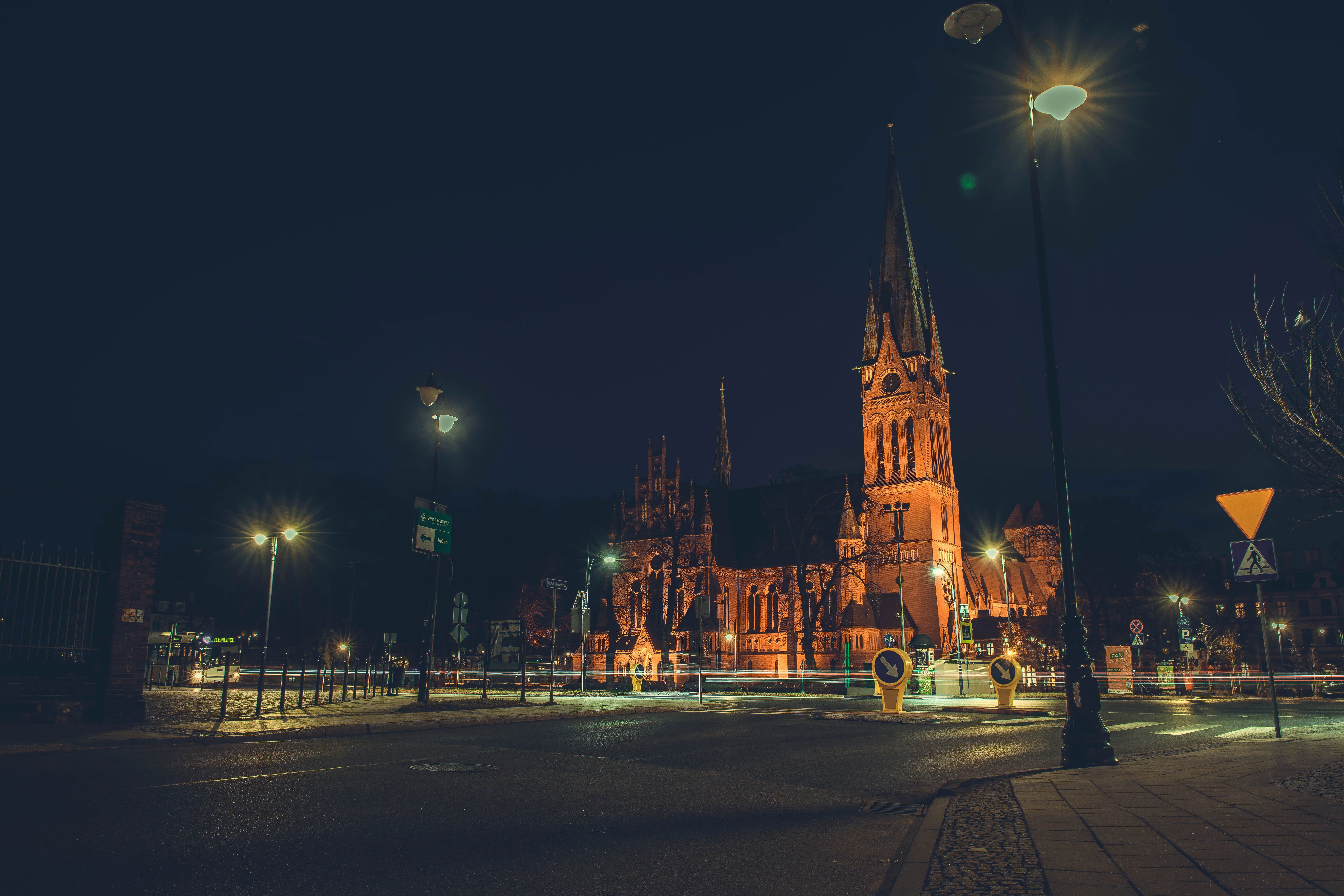Children with paper lanterns walking past a lit church tower on a dark November evening