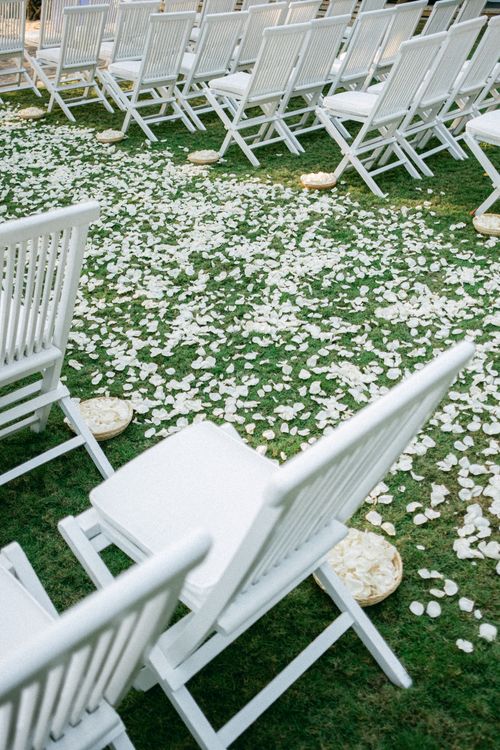Free Elegant outdoor wedding ceremony setup featuring white chairs and rose petals on grass. Stock Photo
