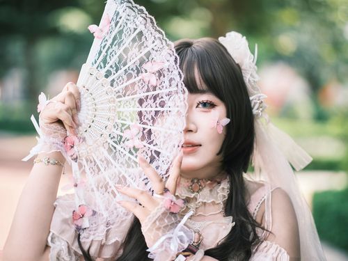 Free Graceful young woman in Lolita attire holding an ornate lace fan, creating a dreamy, elegant look outdoors. Stock Photo