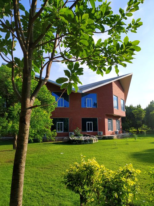 Free A contemporary red brick house surrounded by lush green lawn and trees under a clear blue sky. Stock Photo