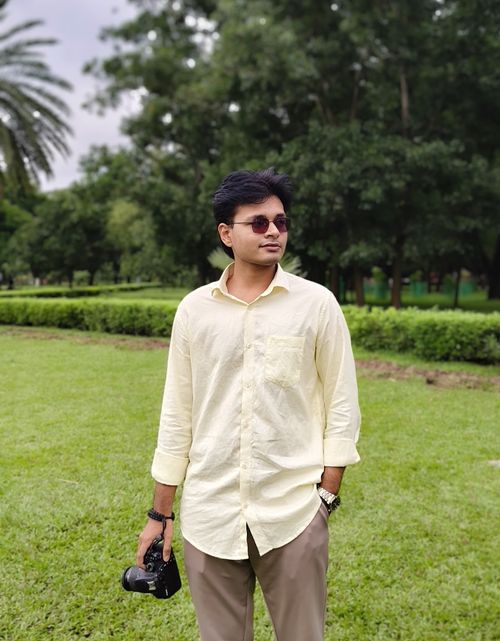 Free Confident young man in sunglasses holding a camera in a lush green park. Stock Photo