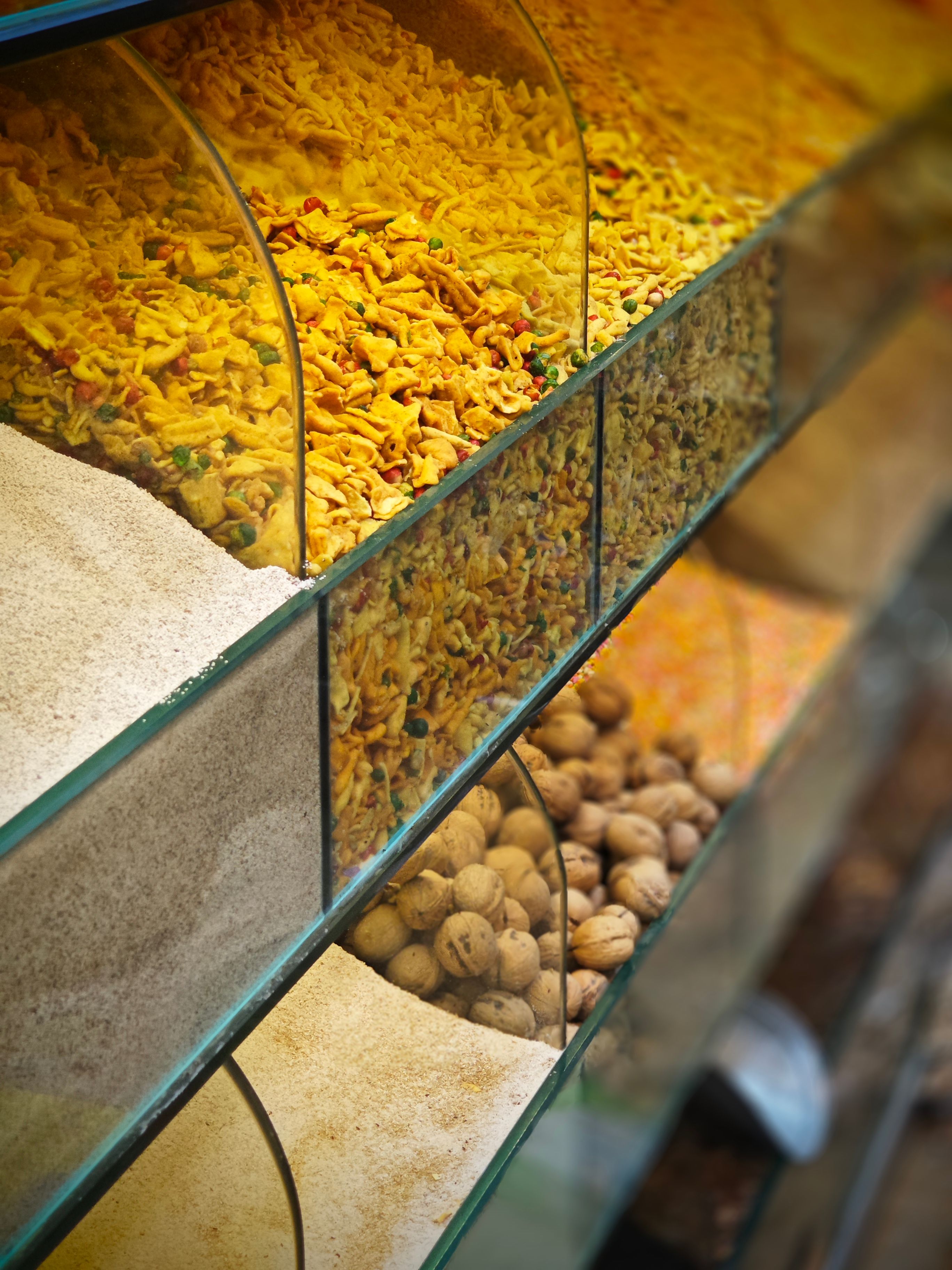 Vibrant spices and nuts arranged in a glass display at a market.