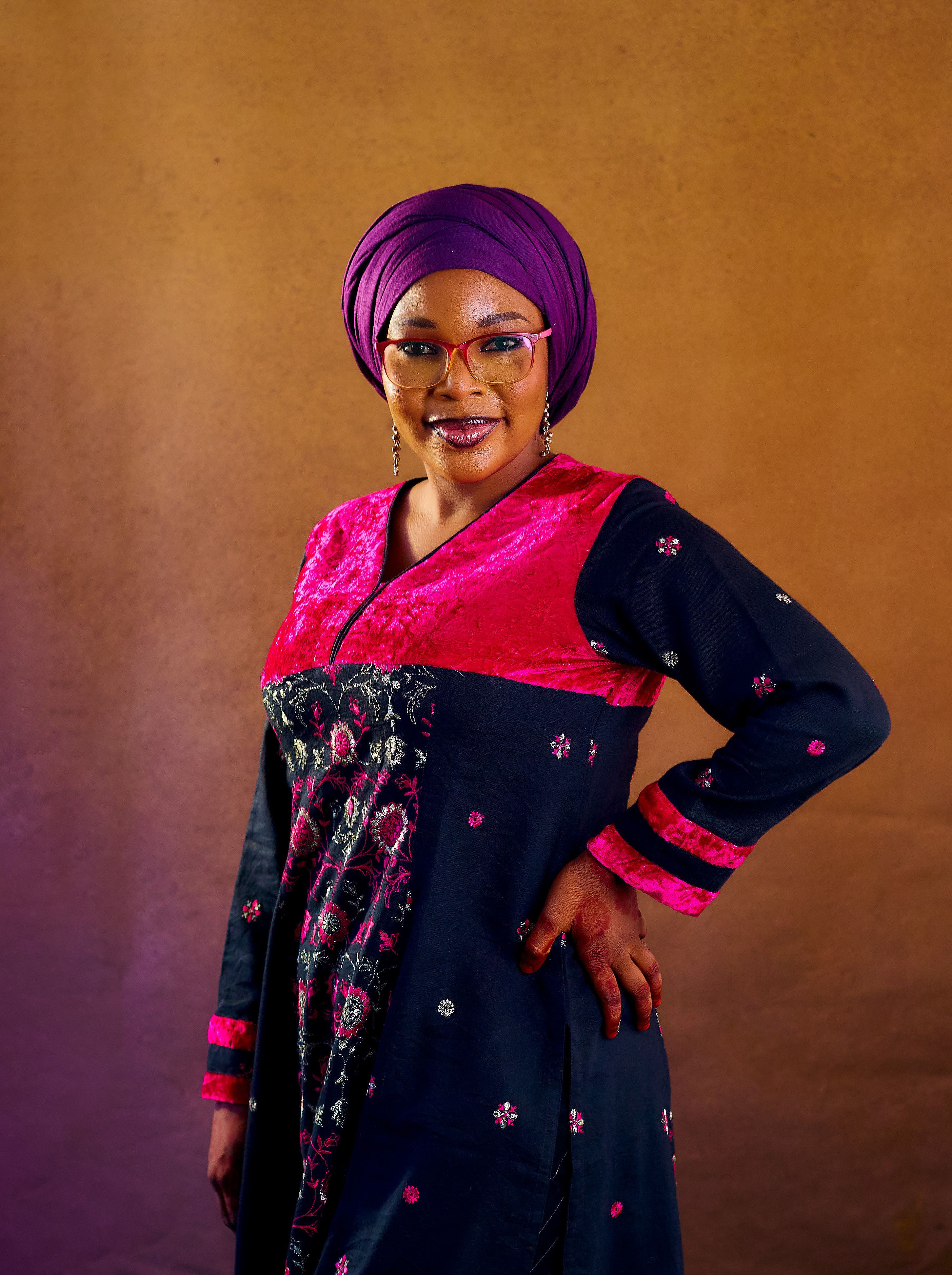 Confident woman posing in colorful traditional African dress on a plain background.