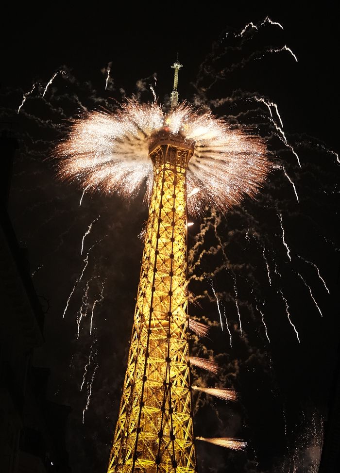 The Eiffel Tower lit up at night with fireworks overhead