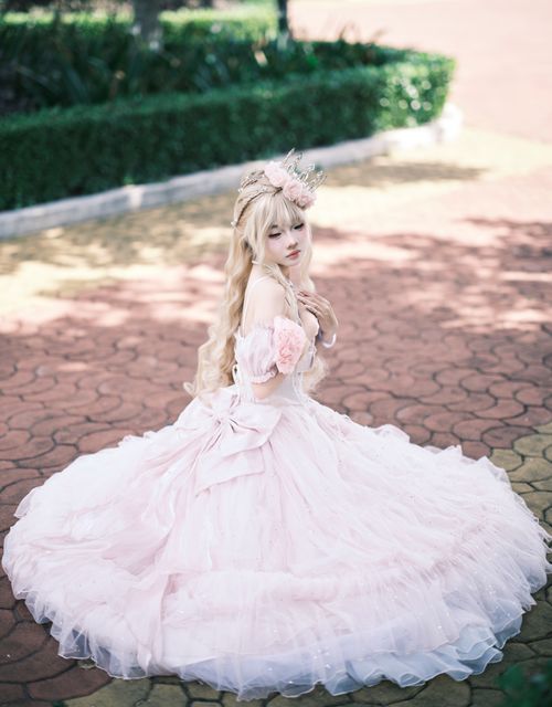 Free Sophisticated woman in pink ball gown seated on patterned pavement in natural light. Stock Photo