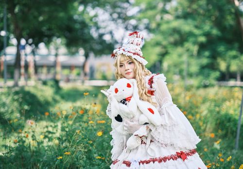 Free A cosplayer dressed in whimsical attire poses outdoors with a plush toy among flowers. Stock Photo