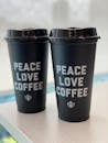 Similar black takeaway plastic glasses with PEACE LOVE COFFEE inscriptions and shiny lids on wooden table for breakfast in morning