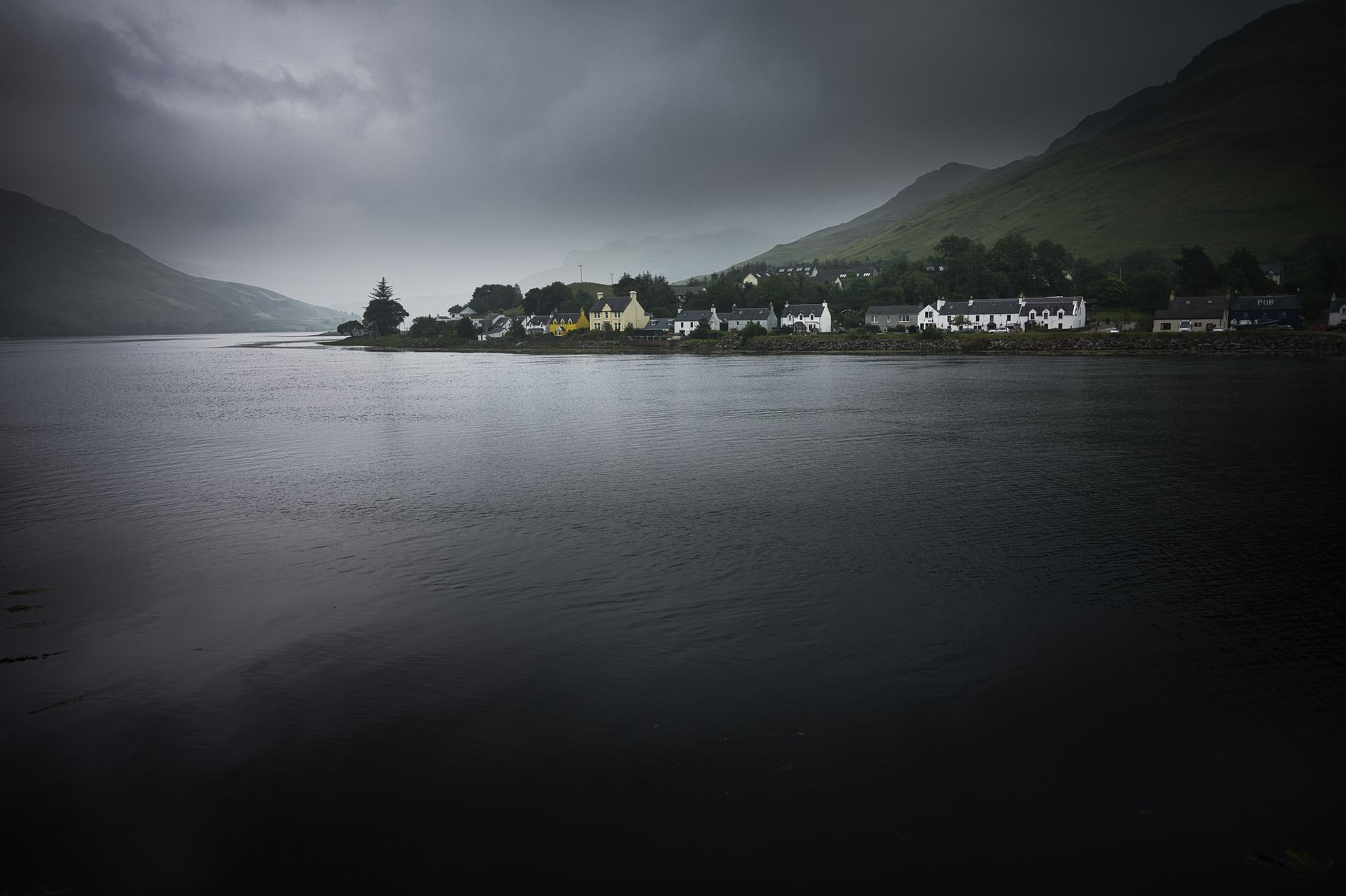 Beautiful view of a Scottish village along the shore of a loch under cloudy skies.