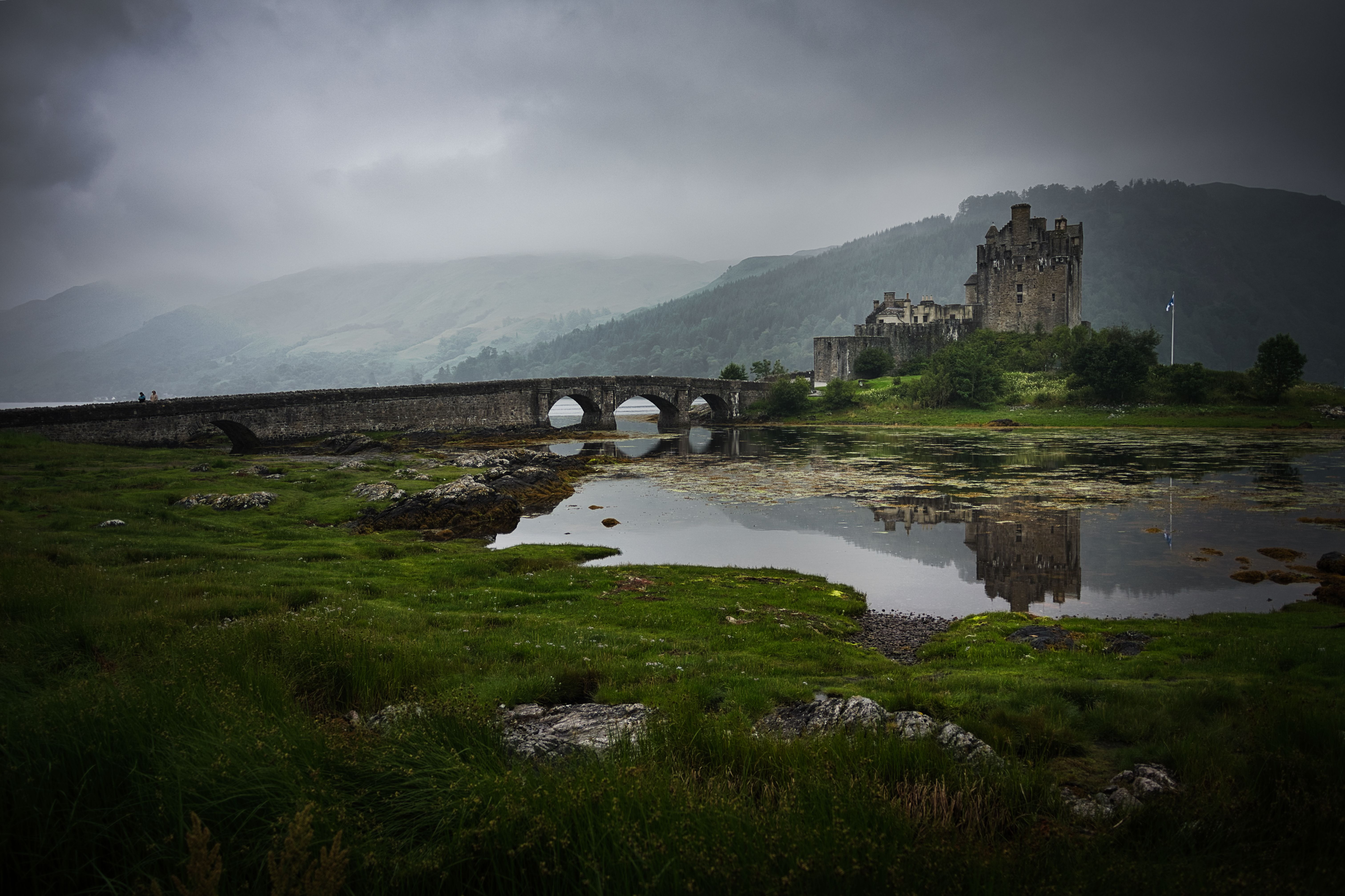 Eilean Donan Castle reflecting in a misty loch with a stone bridge in Scotland.