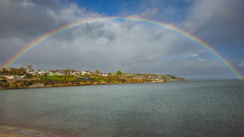 Free A vibrant rainbow arches over a scenic coastal village by the sea, enhancing the natural beauty. Stock Photo
