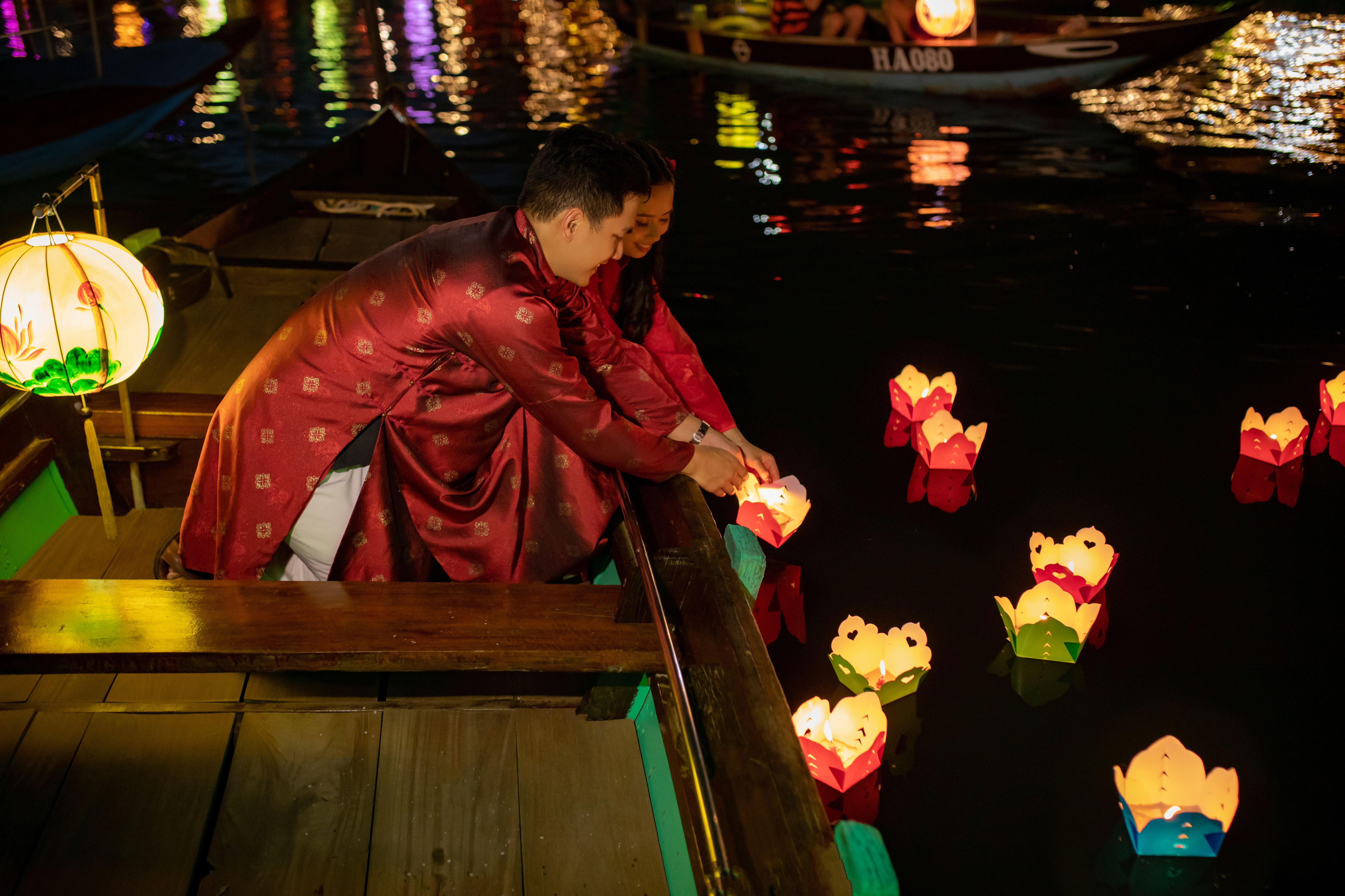 A couple in traditional attire releases floating lanterns into the water during a night celebration in Đà Nẵng, Vietnam.