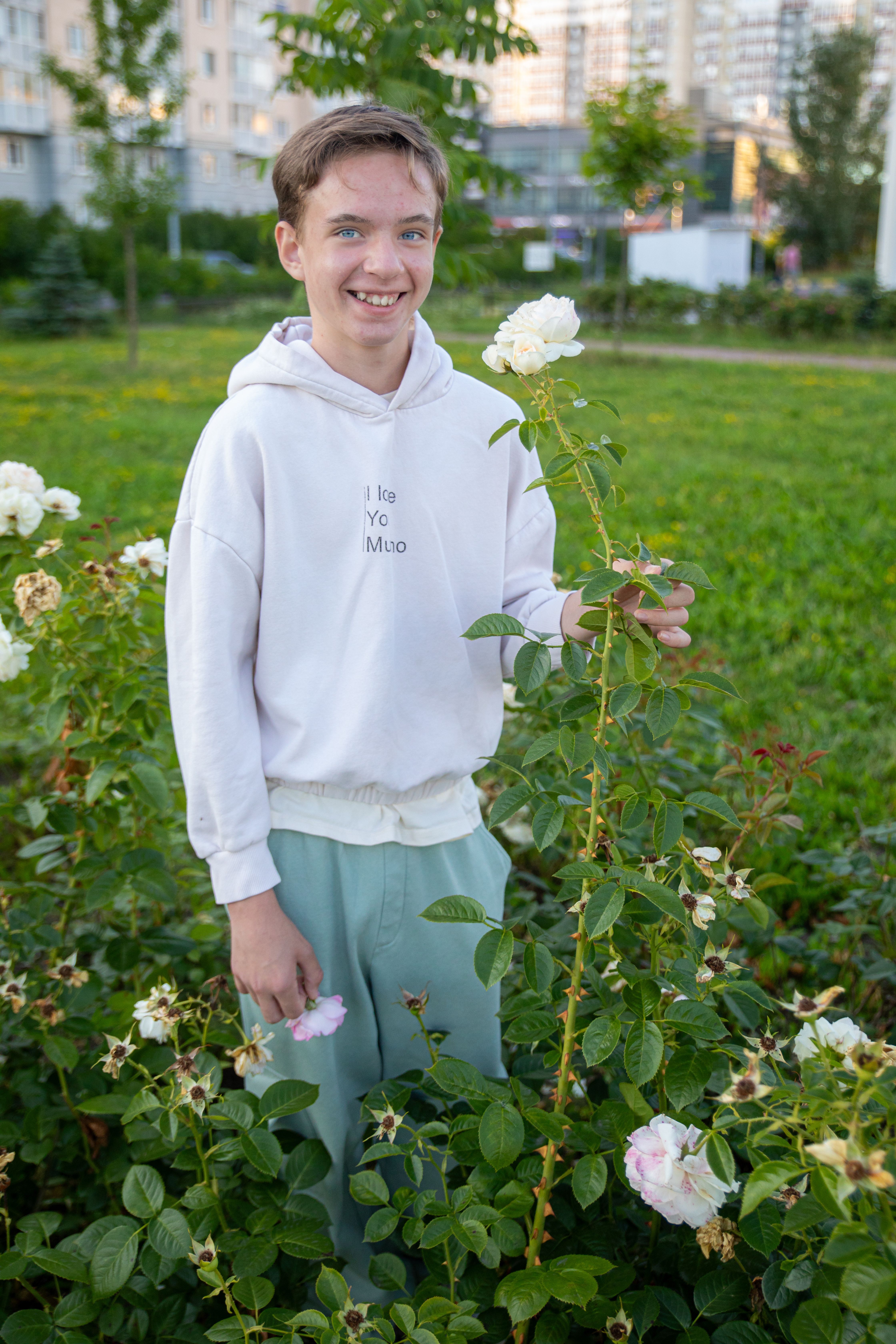 Teenager in a city garden surrounded by blooming roses, embodying carefree lifestyle.