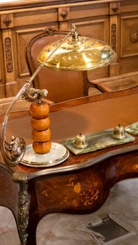 Vintage wooden desk with a brass lamp in a classic setting, ideal for elegant interiors.