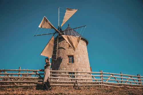 Free A woman stands near a traditional windmill in the countryside of Ankara, Turkey, on a sunny day. Stock Photo