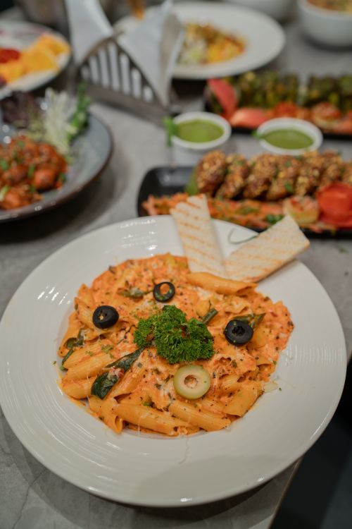 Free Creamy pasta with olives, parsley, and side dishes on a table setting indoors. Stock Photo