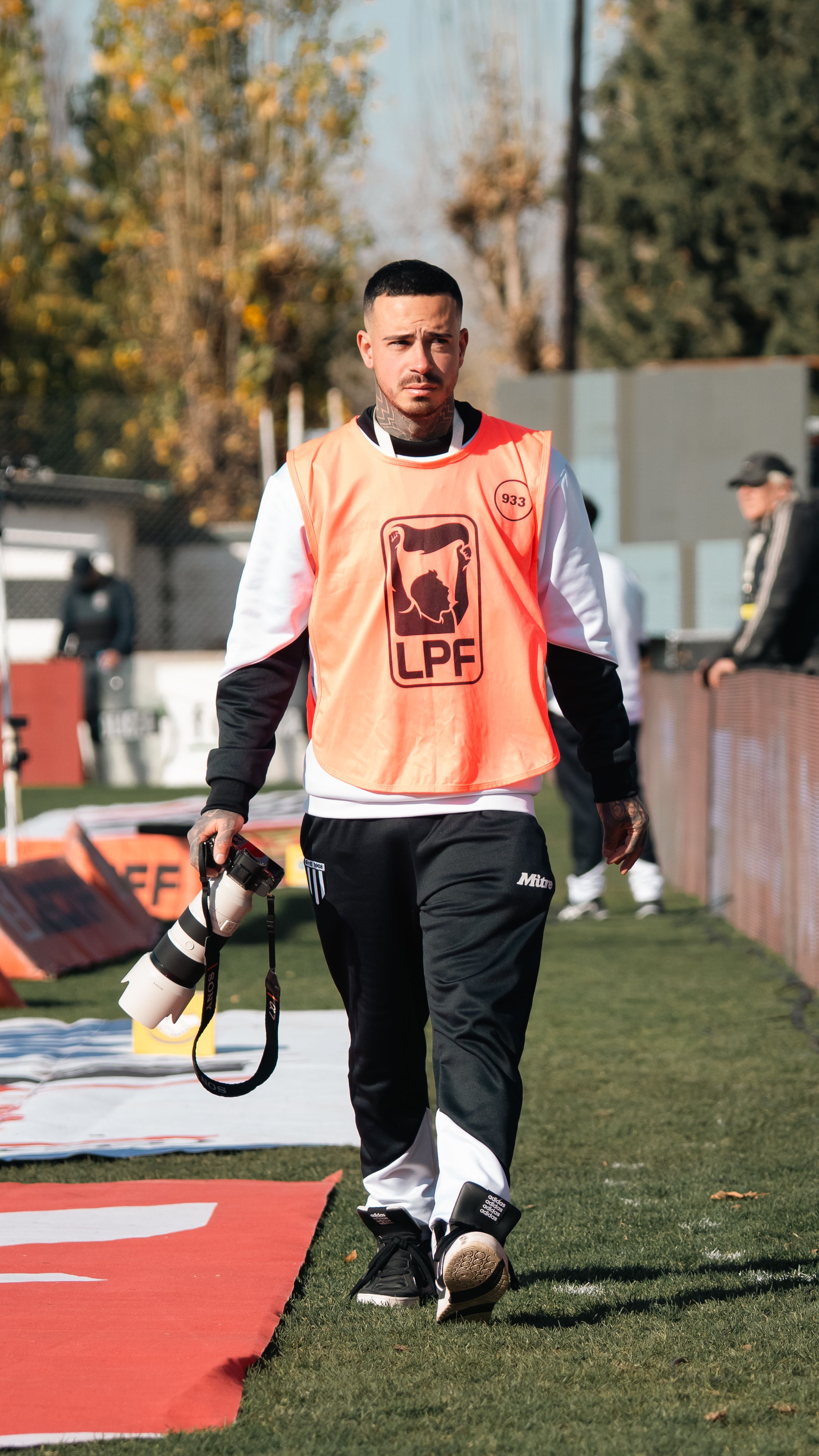 Photographer with camera at a sports event wearing orange vest during the day.