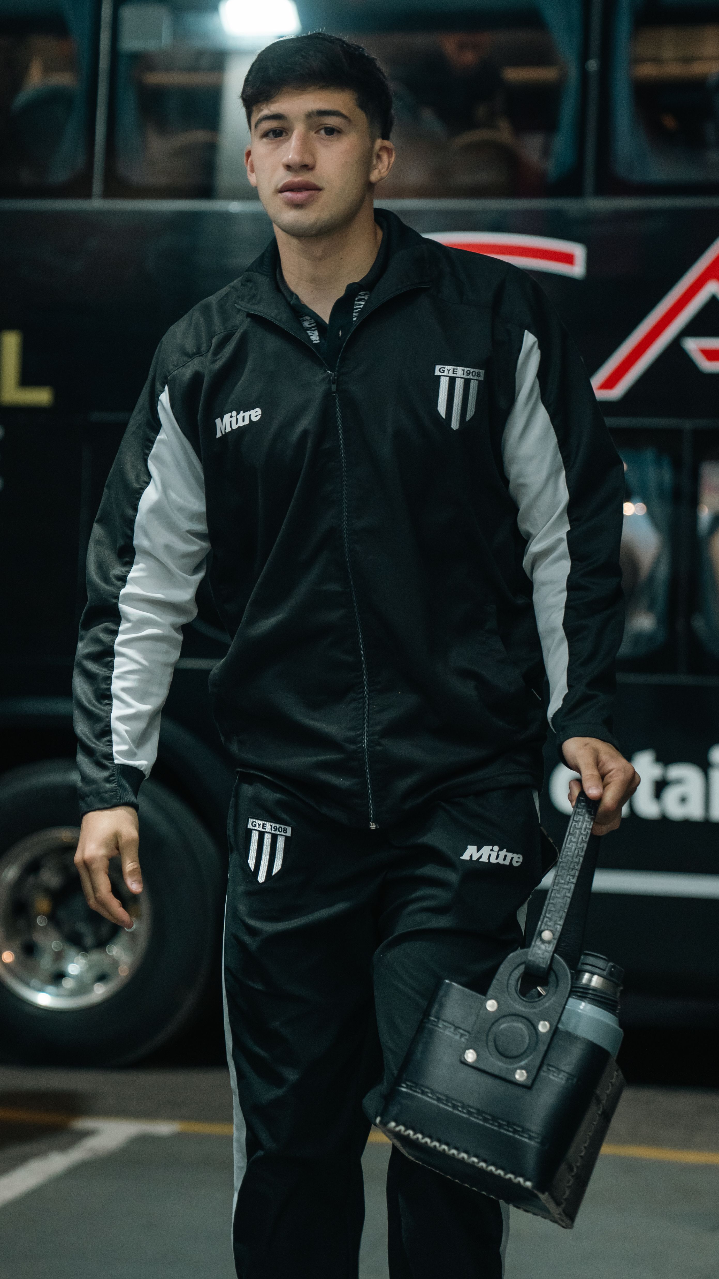 A young male athlete dressed in a black tracksuit, arriving at a sporting event.
